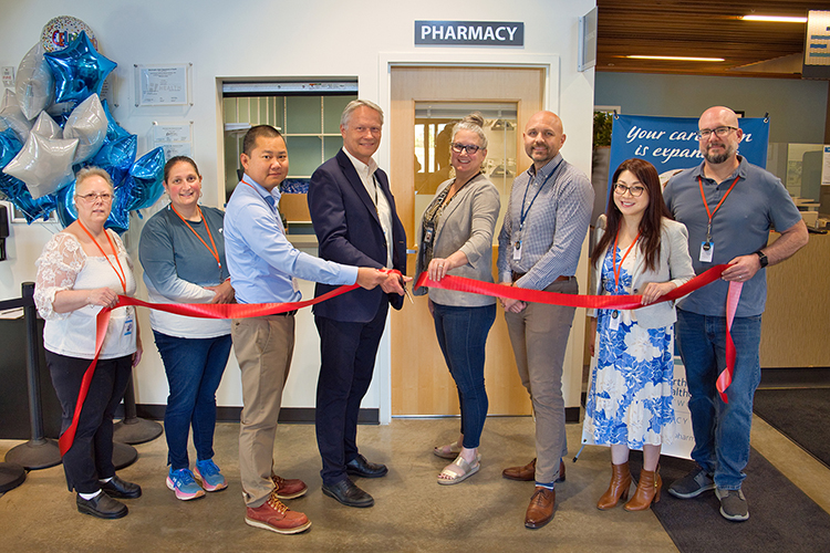 Leadership and pharmacy staff holding and cutting a red ribbon in front of new NOHN Pharmacy office at the Downtown Health Center.